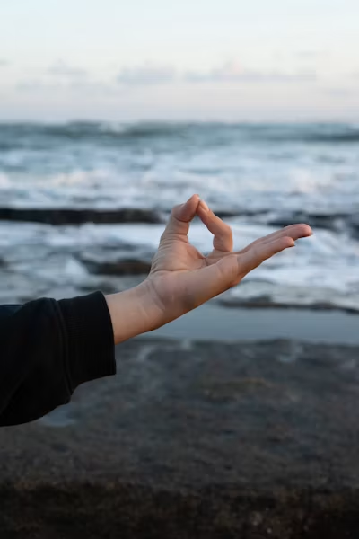 Hand forming a mudra by the ocean